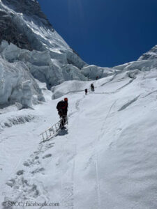 The Icefall Doctors ascend in the Khumbu Icefall. One of them pulls a ladder behind him. 
